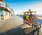Family pedaling a surrey on the boardwalk at the beach.