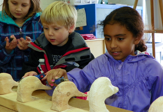 children looking at wooden duck head carvings